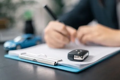 Persona firmando documentos con llaves de auto y un auto de juguete sobre la mesa.