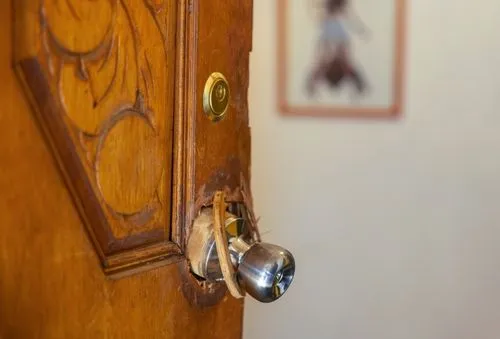 Close-up of a wooden door with a broken doorknob after a forced entry.