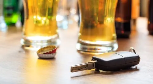Llave de auto sobre una barra de bar junto a dos vasos de cerveza y una tapa de botella.