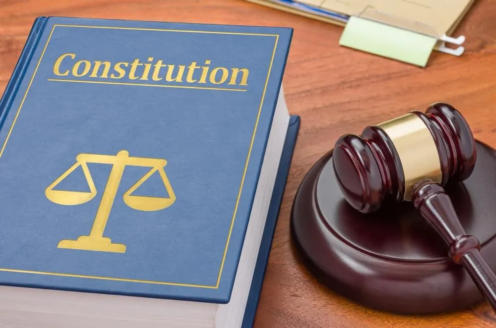 Un mazo descansa sobre un libro de leyes titulado "Constitución", simbolizando la justicia y la autoridad legal.