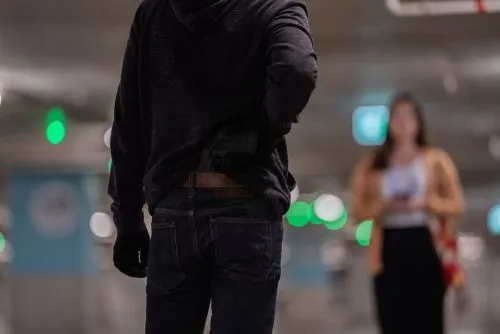 A man conceals a handgun in his waistband while a woman approaches in a parking garage.