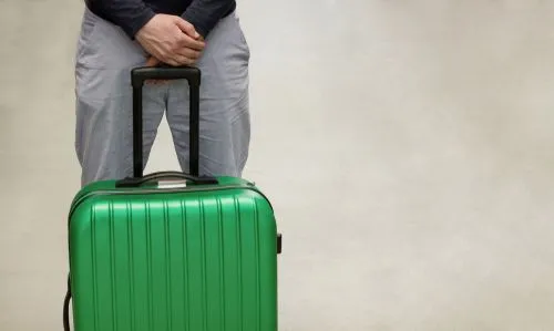 Una persona de pie en un aeropuerto sosteniendo una maleta verde, representando preocupaciones de viaje, inmigración o deportación.