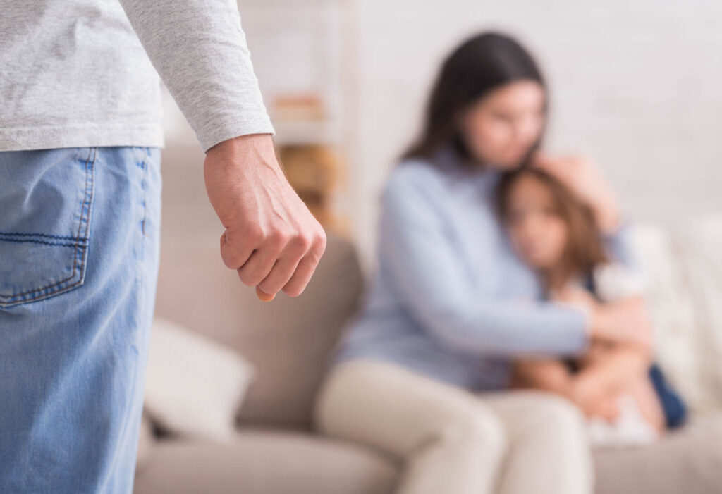 Abuso doméstico. Mujer asustada con su hija pequeña que sufre la violencia de su esposo, puño masculino en primer plano, enfoque selectivo