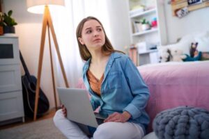 Niña joven preocupada sentada con una computadora portátil