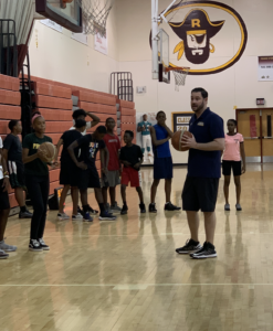 Adam Rossen and a PBSO Deputy running basketball drills with children at the Tri-City Basketball, Academics and Mentoring Camp
