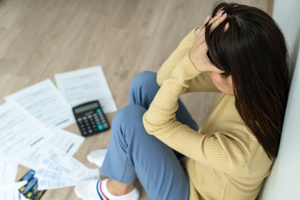 Stressed woman experiencing a headache while managing monthly bills and mounting credit card debt.