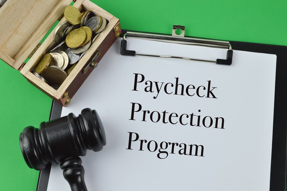 Close-up of stacked coins, a judge's gavel, and a white sheet of paper labeled "Paycheck Protection Program."
