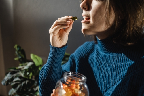 Woman in a blue sweater holding a jar of gummies and about to eat one.
