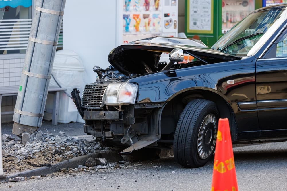 A car with severe front-end damage after crashing into a utility pole, which is now left leaning from the impact.