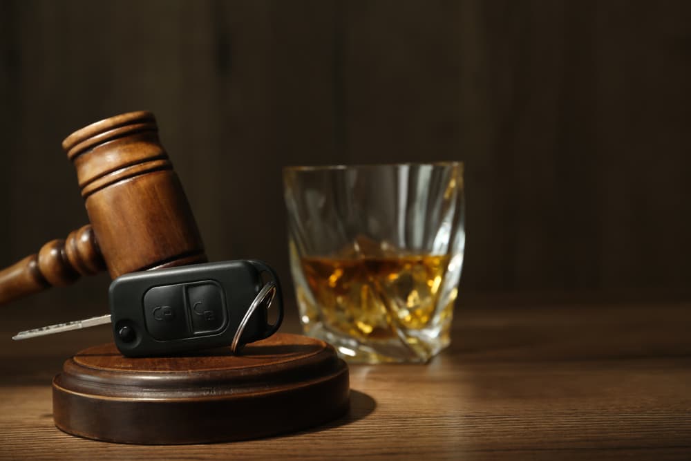 Car key, gavel near glass of alcohol on wooden table